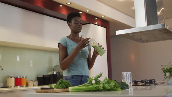 Smiling african american attractive woman tasting homemade smoothie in kitchen