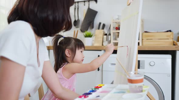 Asian young happy kid daughter coloring on painting board with mother.