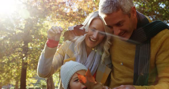 mom dad and daughter holding leaves and smiling outdoors