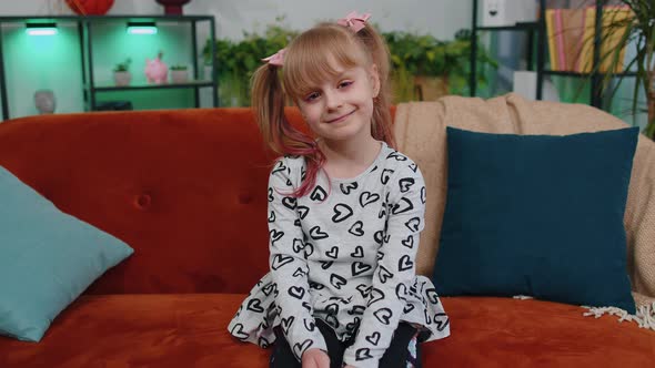 Cheerful Lovely Caucasian Little Toddler Kid Girl Smiling Looking at Camera Sitting on Sofa at Home