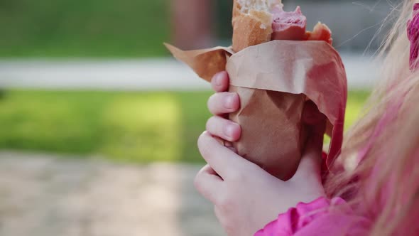 Little Girl Biting Hot Dog Outside on Sunny Day