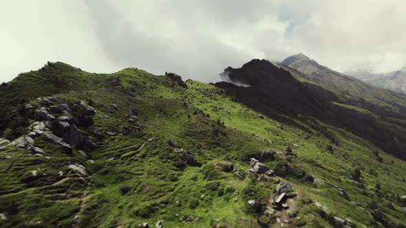 Aerial drone shot of a grass covered mountain top with a small trail leading along with a person hik