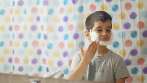 Little Boy with Shaving Foam on Face Looking Into Mirror in Bathroom