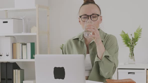 Young Female Between 30 and 40 Years Old Drinks Water in Front of Pc