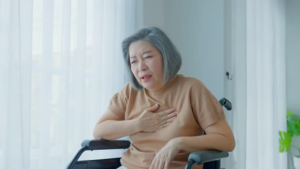 Asian Senior old disabled woman with chest pain suffer from heart attack on wheelchair in house.