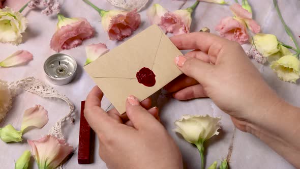 Hands taking wax sealed envelope from a marble table near pink flowers