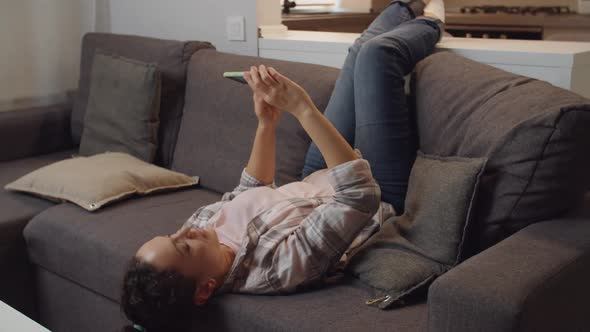 Adult Woman Taking Selfie Using Mobile App While Lying on Couch Indoor