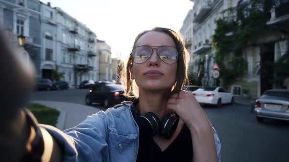 A Young Girl in Glasses Poses with a Camera on Her Outstretched Hand