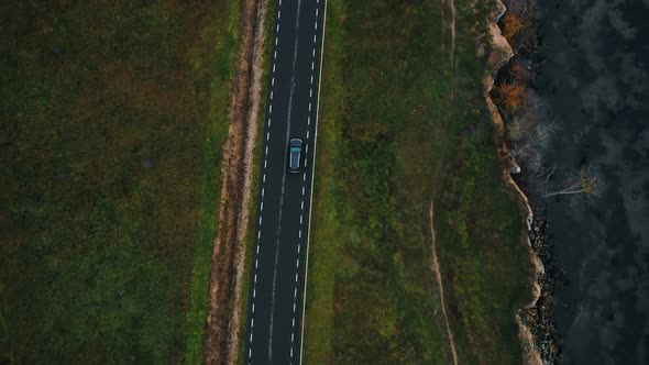 Aerial Top View Tracking Shot of Black Car Moving Along Epic Highway Road Along Old Autumn Eroded