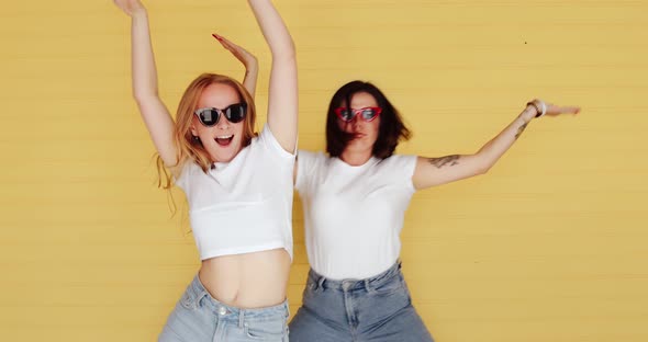 Beautiful two women blonde and brunette dancing funny crazy dance on a yellow background