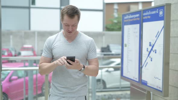 Young Tourist Man Using Phone and Taking Selfie in Front of Map at Train Station in Bangkok