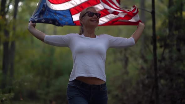 Pretty, mature woman wearing sunglasses and smiling pulls an American flag up over her head and them