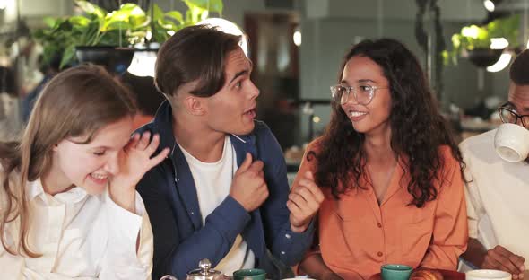 Handsome Guy Gesturing and Telling Funny Story While Sitting with Multiethnic Coworkers in Cosy