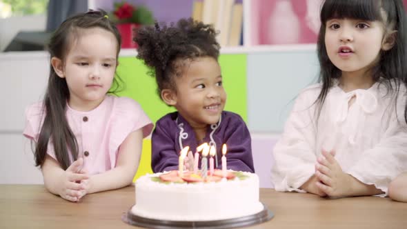 Multi-ethnic young girls happy make a wish blow out candles on birthday cake at school.