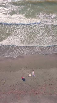 drone, a woman and two men are sunbathing and relaxing on an empty beach by sea.