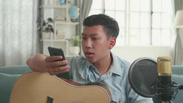 Asian Boy Vlogger With Guitar Read Comment On Mobile Phone While Streaming