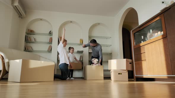 Happy Young Parents and Daughters Run Push Cardboard Boxes with Dog Pets Dog Jack Russel Ride Inside