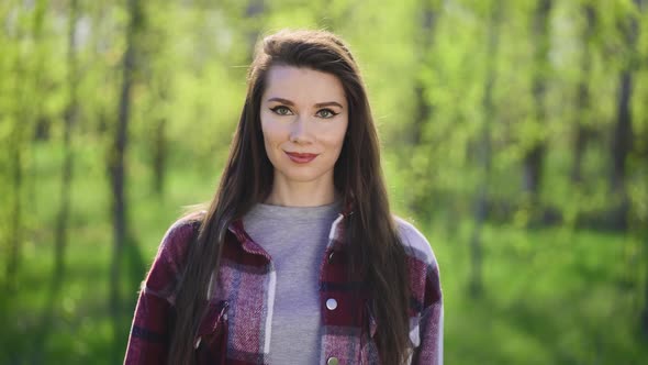 Portrait of a Young Brunette on a Background of Green Trees