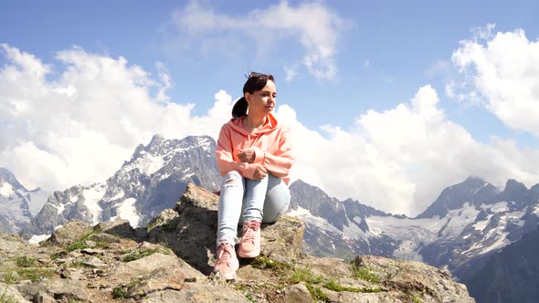 Young Woman Sitting on Rock and Looking at Mountain Landscape