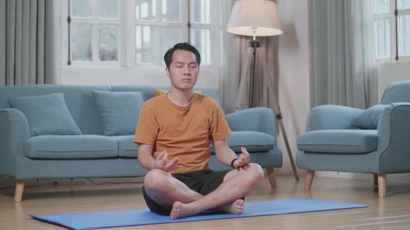 Asian Man Doing Yoga In Easy Pose On Mat At Home