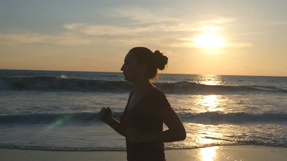 Girl Jogging Along Ocean Shore During Sunrise. Silhouette of Young Woman Running on Sea Beach at
