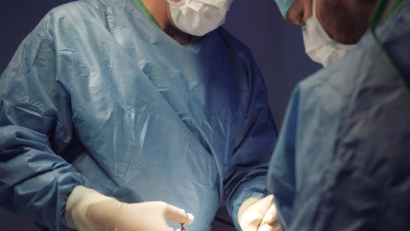 Doctor's Face in a Medical Uniform and a Mask Makes an Operation in the Operating Room