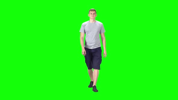 Young Man in a Grey T-shirt, Shorts and Sneakers Going Against a Green Background. Slow Motion.