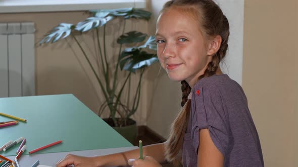 School Girl Smiling To the Camera Over Her Shoulder While Drawing