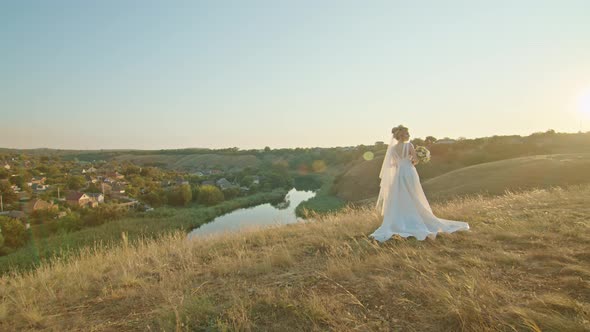 Happy Young Woman Bride at Sunset Standing on a Mountain Hill Enjoying a Pleasant View of the River