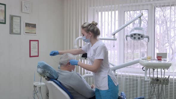 Dentist Assistant in Protective Mask Preparing Elderly Patient to Examination in Dental Clinic