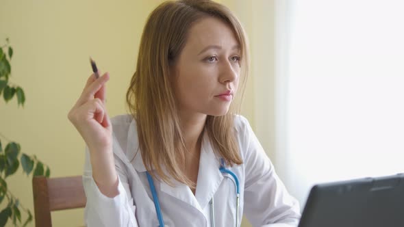 A nurse in a bathrobe and with a stethoscope works at a laptop