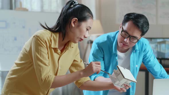 Asian Woman And Man Engineers Holding Paper Model Of House Discuss About Design At The Office