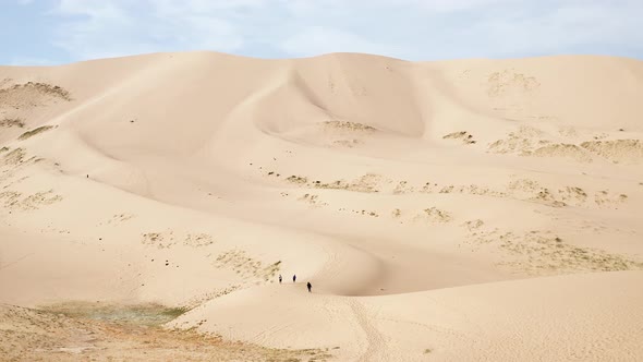 Aerial dolly of three people walking on sand dune in gobi desert in daytime
