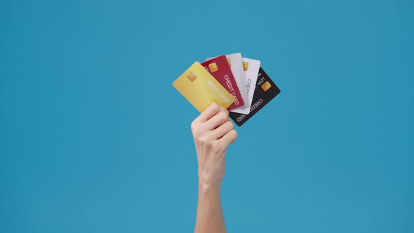 Young woman hand shows credit card for shopping online over blue background in studio.