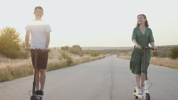 Couple in Love Riding on Electric Scooters Smiling to Camera on Way Out of Town