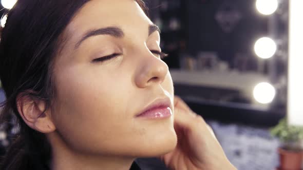 Make Up Artist's Hand Applying Foundation on Previously Prepared Face of an Attractive Brunette Girl