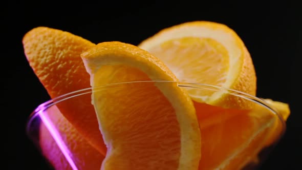 Oranges In A Martini Glass Rotate On A Black Background In A Purple Hue In The Center Close