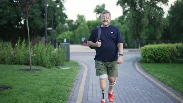 Front View Portrait Confident Greyhaired Male Amputee Walking in Slow Motion in Summer Park Looking