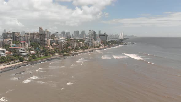 Drone shot of waves crashing on the coast of Mumbai. The sea link is visible in the background.