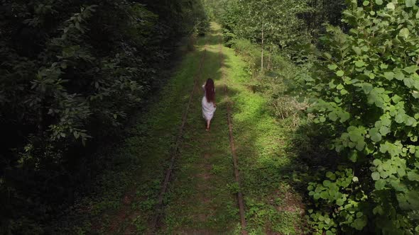 Aerial View of a Young Girl in a White Dress From the Back Walking Barefoot Along an Abandoned