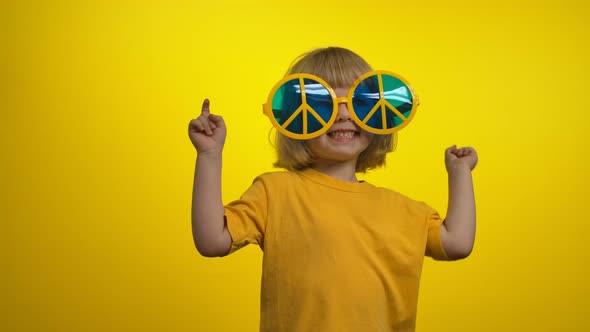 Little Girl in Yellow Sunglasses is Dancing and Smiling on the Yellow Background