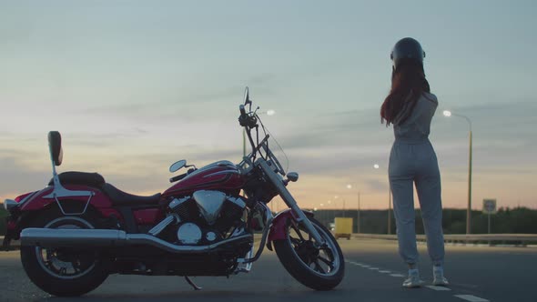 Woman Stands Next to Her Red Cool Motorcycle Removes the Helmet From Her Head Holds It in Her Hands