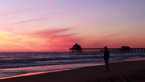 A man enjoys his vacation at the beach during a gorgeous red, purple, tangerine, pink and blue sunse