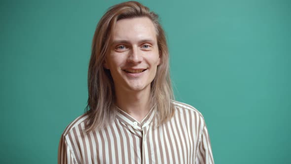 Portrait of Handsome Young Man with Long Hair Smiling at Camera Isolated Over Green Background