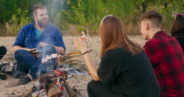 Attractive Multiracial Group Of Young Friends Around Burning Camping Bonfire In The Woods Eating