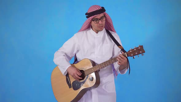 Arab Man Clumsily Plays Acoustic Guitar on Blue Background