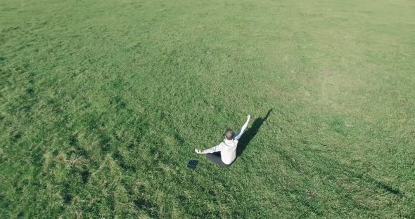 Low Orbital Flight Around Man on Green Grass with Notebook Pad at Yellow Rural Field