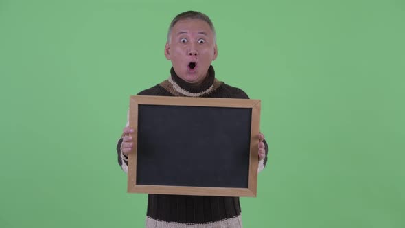 Happy Mature Japanese Man Holding Blackboard and Looking Surprised