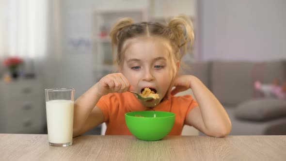 Happy Little Girl Eating Cornflakes With Milk Sitting Home Table, Healthy Food