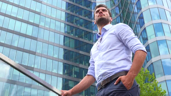 A Businessman Stands in Front of an Office Building and Looks Around Proudly, Closeup From Below